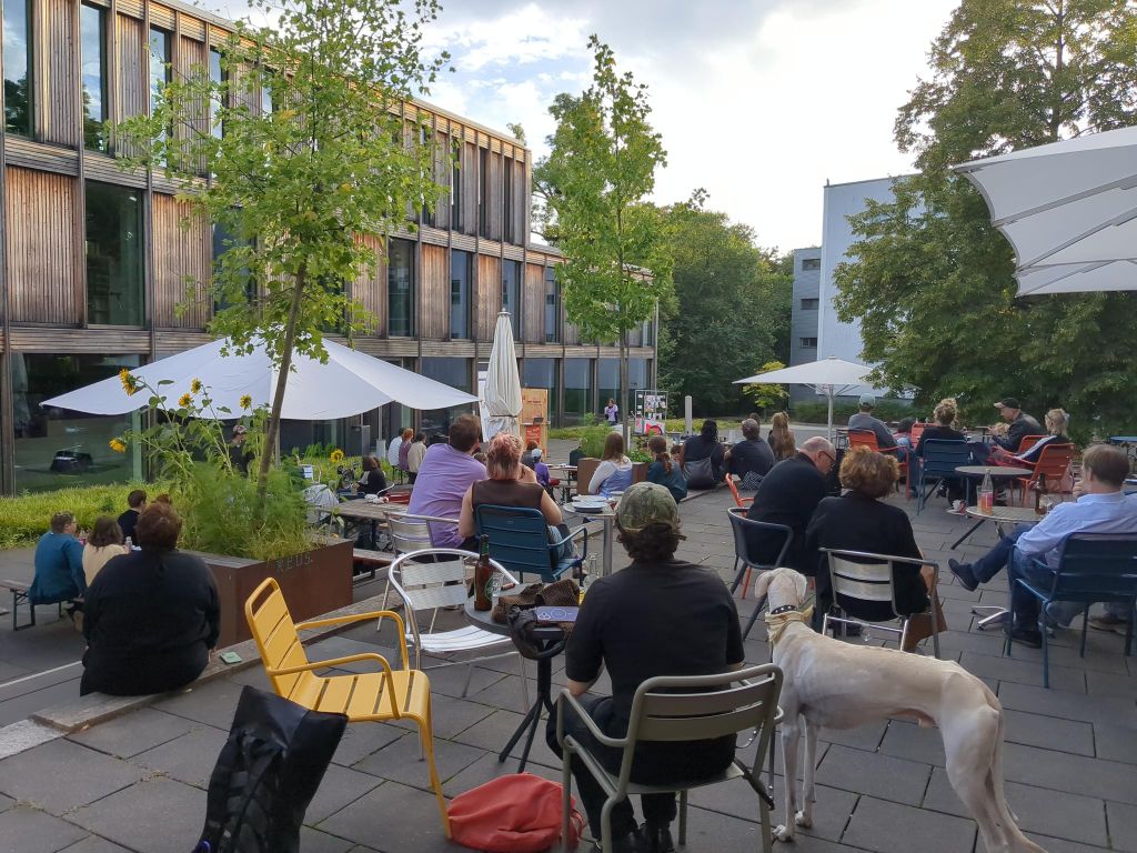 Einige Personen sitzen auf Stühlen auf dem Campus der Burg Giebichenstein und hören einer Person am Mikrofon zu
